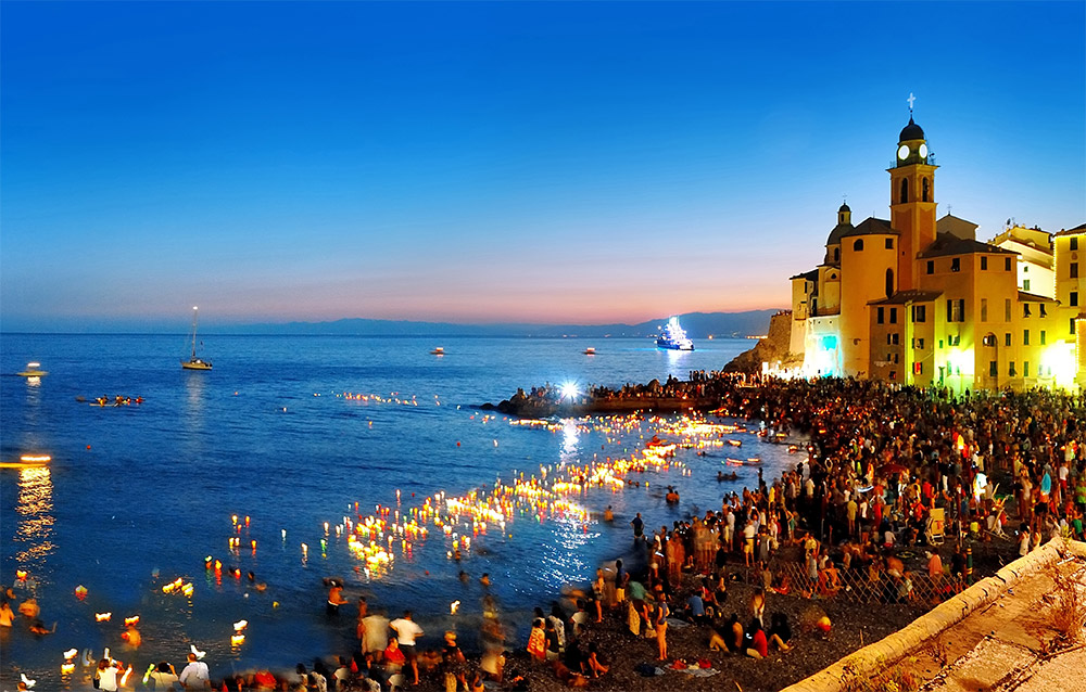 Gente con lumini in spiaggia di notte a Camogli